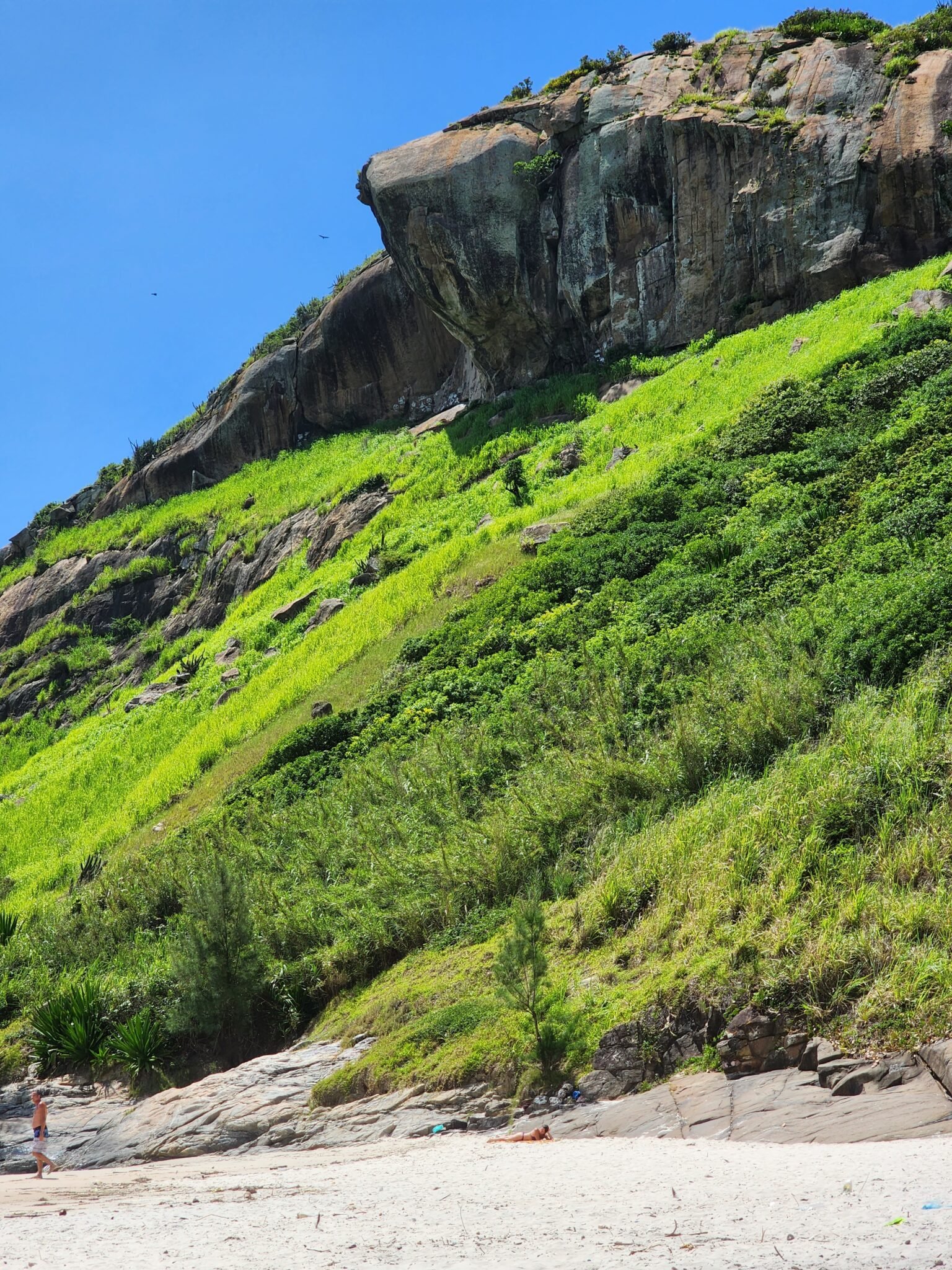 Vista panorâmica da Pedra da Tartaruga em Barra de Guaratiba, Rio de Janeiro, com céu azul e mar cristalino ao fundo.